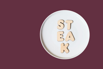 The word Steak made of wooden letters on a round white plate