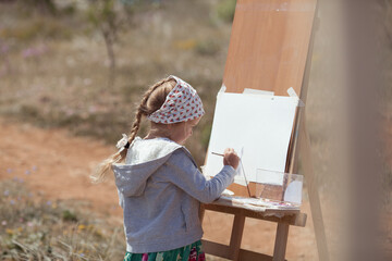 The girl draws in the park on an easel, plein air. Child learns to draw in nature