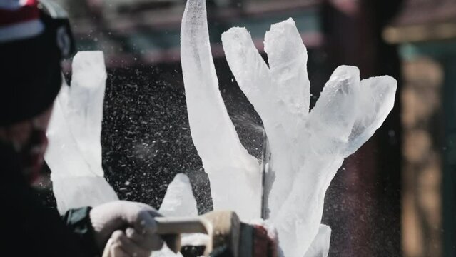 Over the shoulder shot of artist shaping antlers out of ice. Close up, slomo
