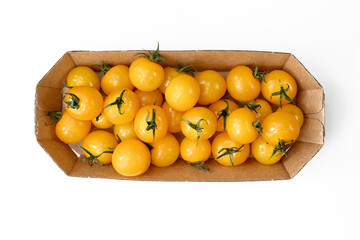 Yellow tomatoes are stacked in a cardboard container on a white table. Flat lay, top view, close-up, macro, can be used for background.