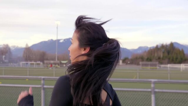 Asian woman in workout clothes running on athletics track. Close up tracking shot