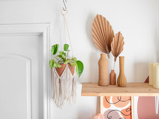 A cotton macrame is hanging beside a wooden shelf and various decor.