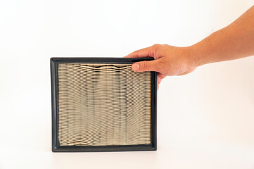 The mechanic's hand grabs the top edge of the used Paper air filter of car engine isolated on white...