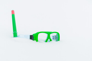 Snow fun. Green diving goggles,snorkel on white snow.Scuba snorkeling green diving set flat lay on the snow at cold winter day.Diving equipment.Copy space.