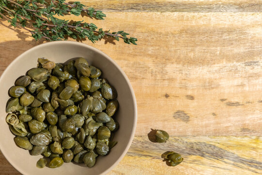 Salted capers in beige bowl over wooden background.