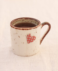 White ceramic mug decorated with a small floral heart on white textured background, tablecloth. Copy space, instagrammable. Coffee drinking with love