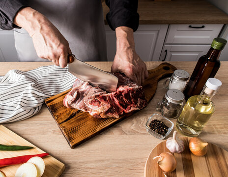 a faceless picture of a man in a gray apron with an axe cuts a large piece of beef on the bones. the concept of cooking meat in the kitchen at home.