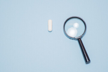 A magnifying glass on a blue background with a place for text and one white pill near the glass: finding a cure, analyzing the benefits and harms of treatment
