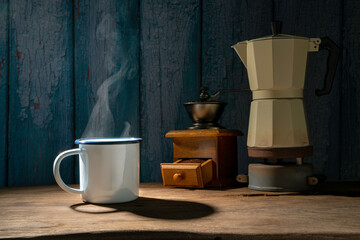 Enameled cup of coffee with smoke.  set of coffee with Moka pot and grinder on the old wooden floor. soft focus.