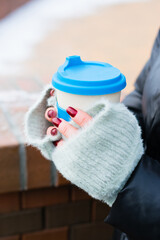 Reusable eco-friendly glass with coffee or tea to go close-up in female hands in winter in the city