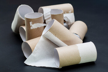 A bunch of empty toilet paper rolls. Cardboard tubes lying in a heap on a dark background. Background on the theme of ecology and recycling of materials.