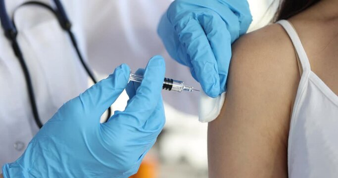 Doctor in gloves holds syringe with vaccine and injects patient in shoulde