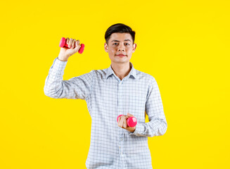 Portrait studio shot of millennial Asian young handsome male sporty athlete model in casual outfit standing look at camera holding two small pink dumbbells lifting exercising on yellow background