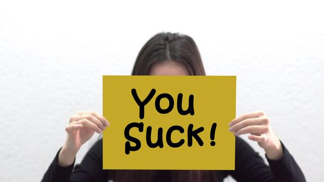 Conceptual message "You Suck" on canvas frame label hold by beautiful girl smiling at camera