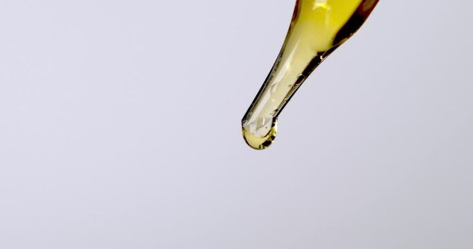 Golden Oil Serum Dripping From Pipette Dropper In White Background. close up