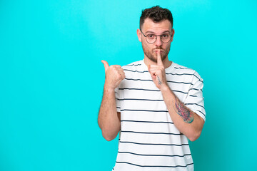 Young Brazilian man isolated on blue background pointing to the side and doing silence gesture
