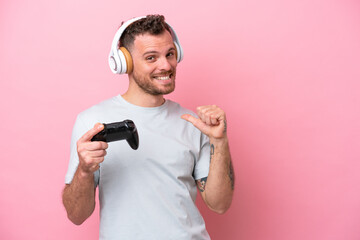 Young Brazilian man playing with video game controller isolated on pink background proud and self-satisfied