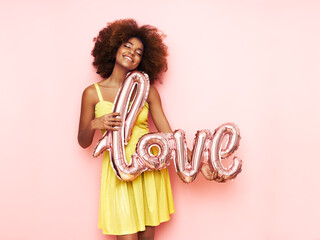 Fototapeta na wymiar A beautiful young African-American woman with a balloon in the shape of the inscription love on a pink background. Woman on Valentine's Day. Symbol of love