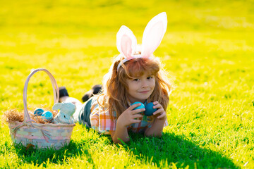 Child boy laying on grass hunting easter eggs. Cute kid in rabbit costume with bunny ears having easter in park. Children hunt easters egg.