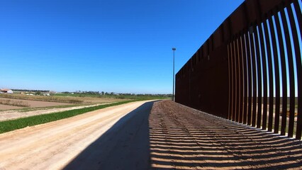 POV driving along the newly built border wall between Texas USA and Mexico; near McCallen Texas; USA farms are visible; concepts of national defense, border security, and Trump's build the wall