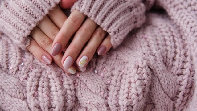 Women's hands with a beautiful matte oval manicure in a warm purple knitted sweater. Winter trend, polish beige nails with gel polish, shellac. 