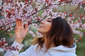 Smiling beautiful girl standing near a peach tree during sunset. Happy face. Spring time.