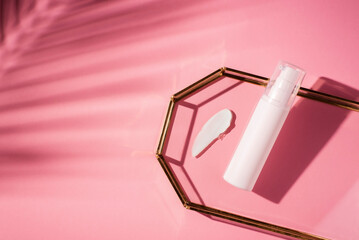 Plastic white tube for lotion with pump and the appearance of the texture of the cream in glass tray on pink bacground. Skin care or sunscreen cosmetic in top view. Beauty concept for face body care