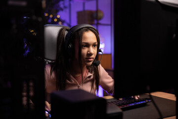 Shot from behind computer monitor of focused gamer. Girl has gaming headset, she is going through...