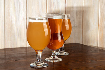 Glasses with different types of craft beer on a wooden bar. In glasses and bottles. Nuts and crackers on the table. On a dark background.