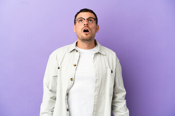 Brazilian man over isolated purple background looking up and with surprised expression