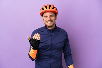 Young Brazilian cyclist man isolated on purple background inviting to come with hand. Happy that you came - obrazy, fototapety, plakaty