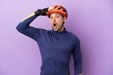 Young Brazilian cyclist man isolated on purple background doing surprise gesture while looking to the side