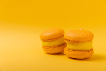 Delicious berry macaroons on a soft yellow-orange paper background. French meringue cookies macaron. Culinary and cooking concept. Copy space. 