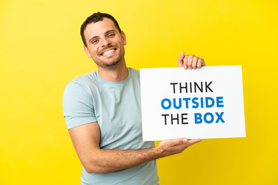 Brazilian man over isolated purple background holding a placard with text Think Outside The Box with happy expression