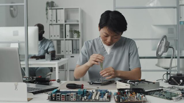 Asian female engineer using laptop and screwdriver while working with chips in laboratory