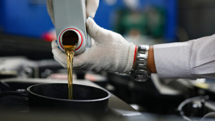 Auto mechanic in gloves pour engine oil into engine