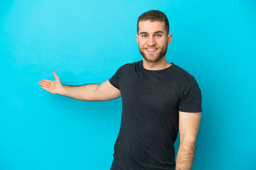 Young handsome caucasian man isolated on blue background extending hands to the side for inviting to come