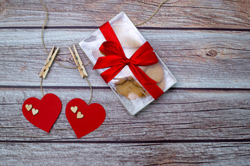 Gift and two red hearts on Valentine's Day. Wedding day. Gift with red ribbon and herarts on wood background with copy space.