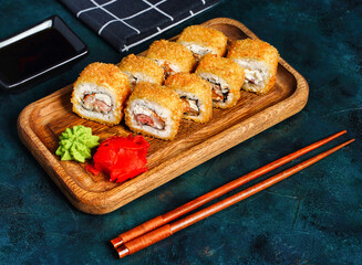 Fried tempura sushi rolls set on wooden plate on dark background. Japanese traditional fusion food...