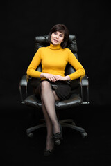 A brunette woman 35-40 years old with a smile is sitting in a huge leather chair on a black...