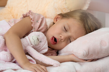 Close up sick little girl lies in bed at home and coughs in sleep. Treatment for illness, flu and cold