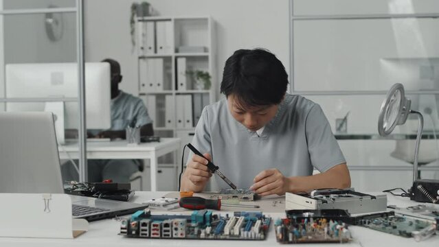 Asian female engineer using soldering iron while making electronic components at worktable in laboratory