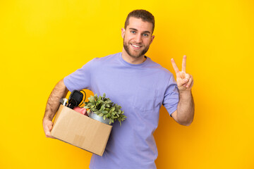 Young caucasian making a move while picking up a box full of things isolated on yellow background...
