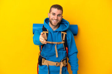 Young caucasian mountaineer man with a big backpack isolated on yellow background shaking hands for closing a good deal