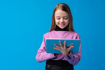 Obraz premium Little girl uses a digital tablet on a blue background