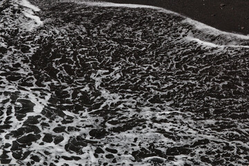 Obraz premium Spray washes over black lava sand