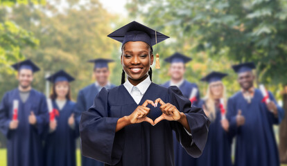 education, graduation and people concept - happy graduate student woman in mortarboard and bachelor gown showing hand heart gesture over group of people on background