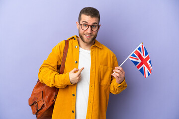 Young caucasian man holding an United Kingdom flag isolated on purple background with surprise facial expression