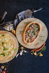 Photo of pizza on a wooden table in a restaurant. Top view. There are various ingredients nearby: cheese, mushrooms, tomatoes