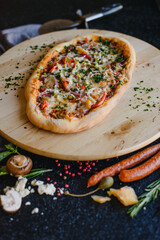 Photo of pizza on a textured wooden table in a restaurant. Top view. There are various ingredients nearby: cheese, mushrooms, tomatoes, spices